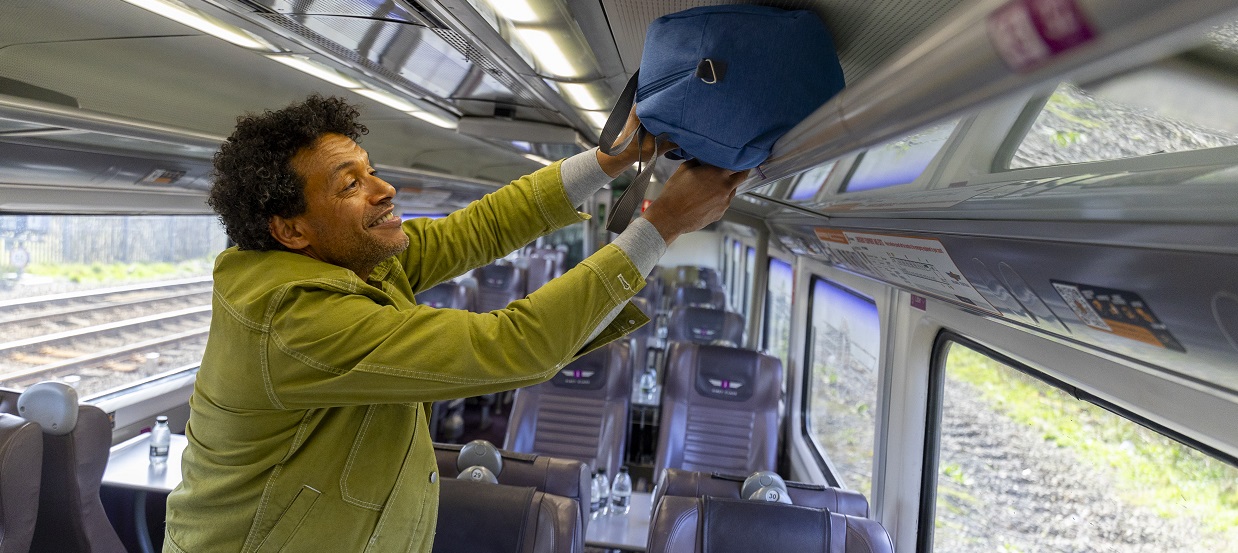 man putting bag in over-head storage on a train