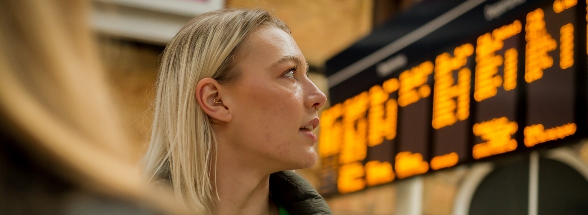 Woman stood in front of train timetable screen.